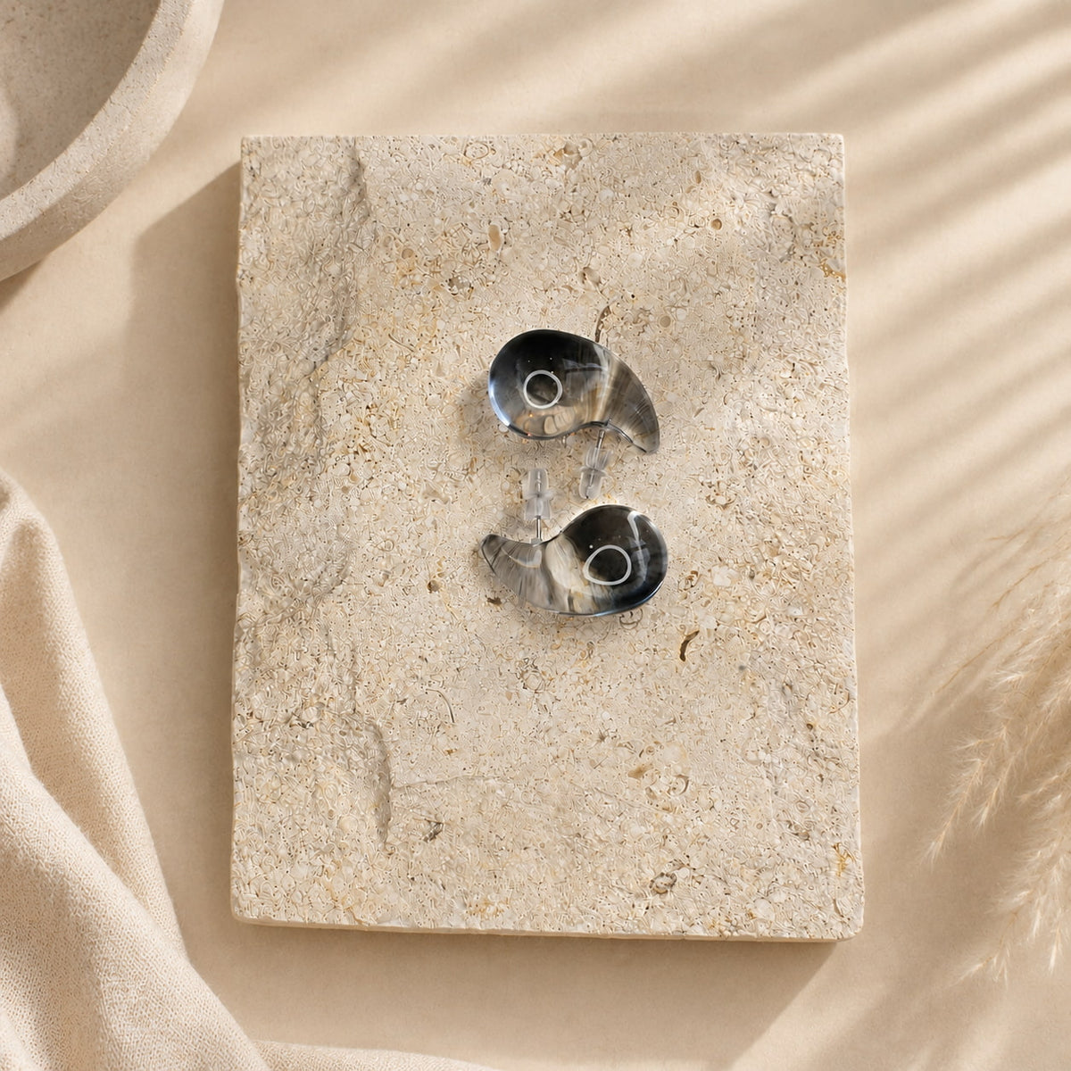 Zwarte semi-transparante oorbellen Charlotte Earrings van hi SISU, flatlay op travertin steen
