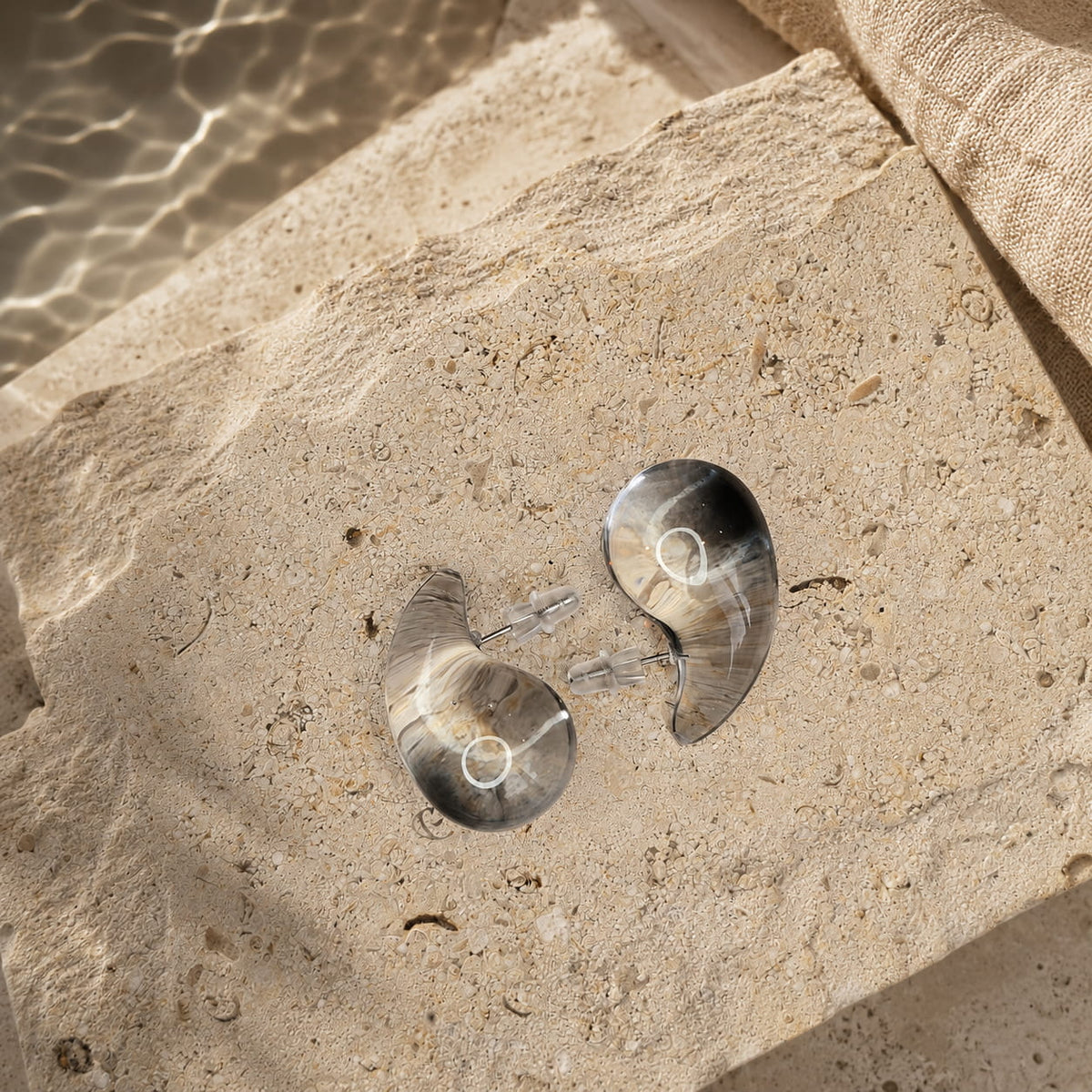 Zwarte semi-transparante oorbellen Charlotte Earrings van hi SISU, flatlay op travertin steen water reflection