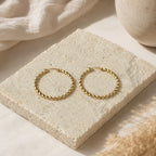Grote goudkleurige twisted hoops Chloe Earrings van hi SISU op travertin steen