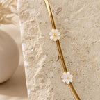 Gouden herringbone ketting met parelmoer bloemen op travertin steen